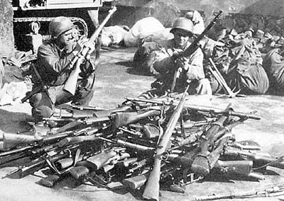 Американские солдаты разряжают трофейное германское стрелковое оружие, представлявшее собой арсенал практически всех оккупированных стран. На переднем плане лежит 7,35-мм итальянская винтовка Маннлихер-Каркано М 1938, получившая в вермахте индекс «Gewehr 231(i)».