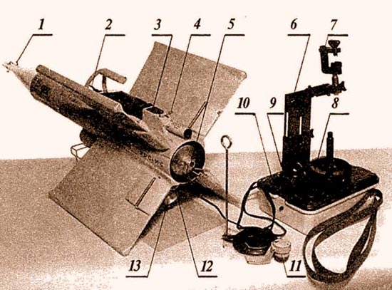 «Кобра» в положении готовности к пуску: 1 – головная часть взрыва-тельного устройства; 2 – транспортировочная рукоятка; 3 – контрольный бортразъем; 4 – стопорный шплинт трассера; 5 – сопло маршевого двигателя; 6–регулируемая по высоте стойка прицела; 7 – струбцина для крепления полевого бинокля; 8 – крышка аккумуляторной батареи; 9 – электро-разъем кабеля управления; 10 – кнопка «пуск»; 11 – бортовой электроразъем кабеля управления; 12 – шунт запальной электроцепи двигателя; 13 – наклонное сопло стартового двигателя. Корпус планера «Кобры» изготовлен из картонной трубы с упрочняющей пропиткой. Корпуса маршевого и стартового двигателей штамованные из алюминиевого сплава. Пластмассовые детали изготовлены литьем из термо-пластичных пластмасс